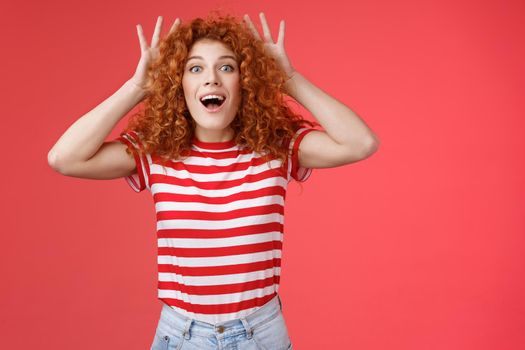 Impressed excited shocked young cute redhead curly-haired ginger girlfriend reacting amazed surprised awesome gift cannot believe own eyes grab head thrilled open mouth ambushed red background
