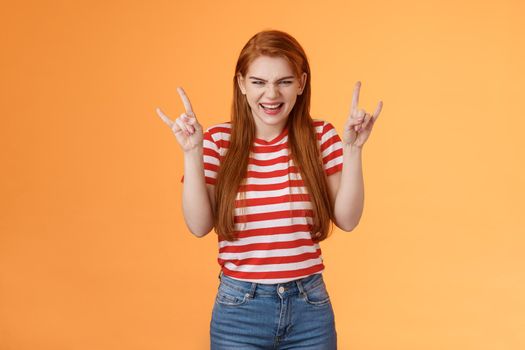 Rebellious sassy good-looking caucasian redhead woman partying having fun, enjoy awesome stunning concert, favorite band, raise heavy-metal signs entertained, smiling sly squinting joyful