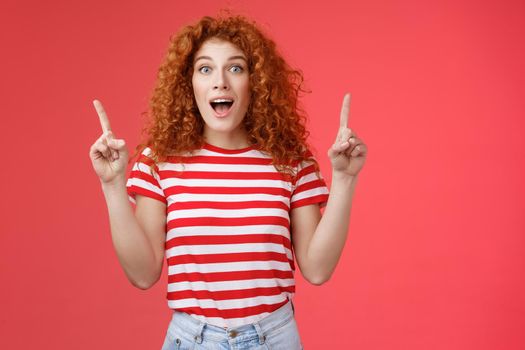 Omg fascinating store check it out. Impressed excited good-looking redhead curly emotive girl drop jaw astonished happy pointing up index fingers directed upwards telling cool news