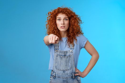You seem familiar. Worried concerned lively redhead emotive curly girl pointing camera look excited nervously recognize someone standing confused hold hand waist wear overalls
