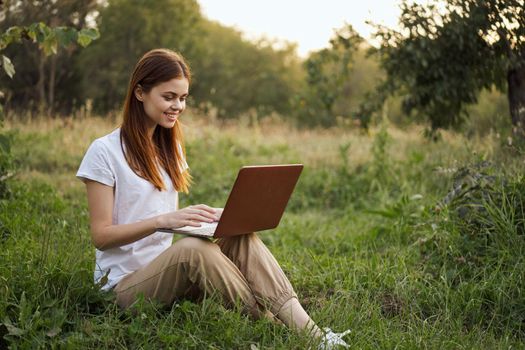 woman outdoors sitting on the grass with laptop summer vacation communication. High quality photo