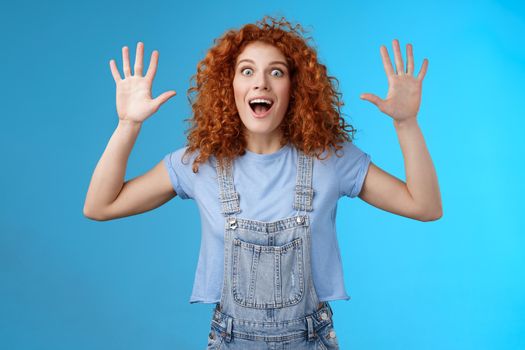 Excited crazy playful funny redhead curly emotive girl yelling carefree raise hands surrender up open mouth fool around smiling broadly stare camera joyful express wild daring emotions
