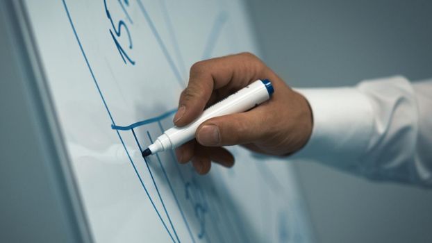Businessman draws diagram with marker on white board. Close up shot of male hand. Toned image