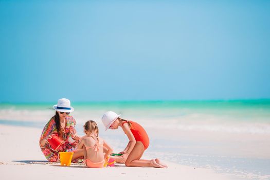 Mother and little daughters making sand castle at tropical beach