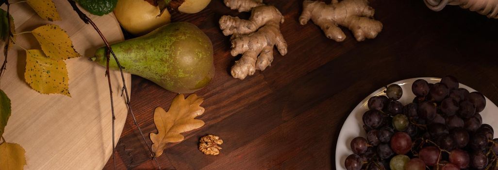 Panoramic banner. Close up top view of a fruits, grapes, ginger root on a wooden table. Wine snacks set: selection of cheese, grapes, pear and walnuts on a wooden board
