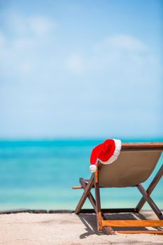 Sun loungers with Santa Hat at beautiful tropical beach with white sand and turquoise water. Perfect Christmas vacation