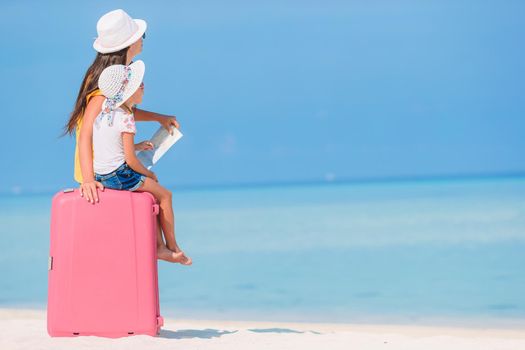 Young beautiful mother and adorable little daughter on tropical beach with baggage and map