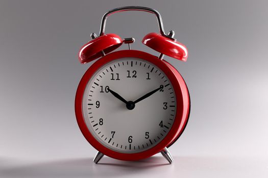 Red classic alarm clock standing on gray background closeup