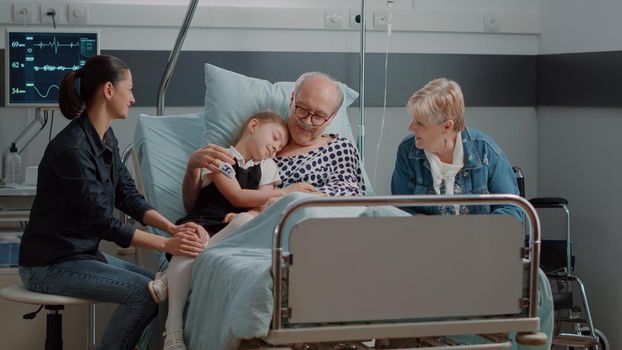 Niece hugging ill grandpa at visit in hospital ward bed