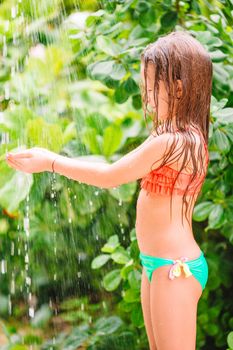 Little happy girl under beach shower on tropical beach
