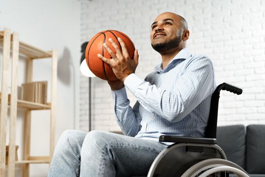 Happy young disabled man in wheelchair holding basketball ball and smiling