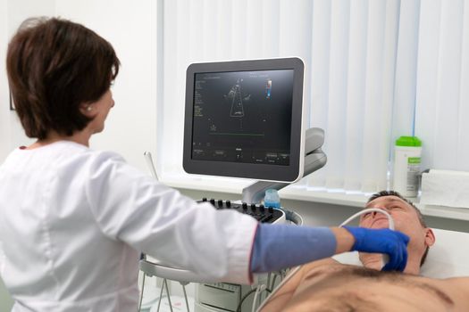 Woman doctor makes heart check of patient man using modern equipment in a cardiology clinic. Female cardiologist is screaning patient heart with ultrasonography, looking at screen. Healthcare concept