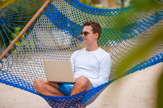Young man with laptop at hammock on tropical vacation