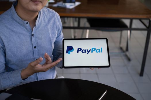 CHIANG MAI, THAILAND - 29 NOV 2021 : Man using Ipad with paypal logo on screen. PayPal is a worldwide online payment system and one of the most popular ways of making payment on the Internet