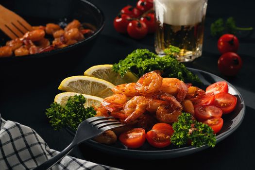 Served dinner - fried shrimp with lemon, tomatoes and herbs and beer in a glass on the table