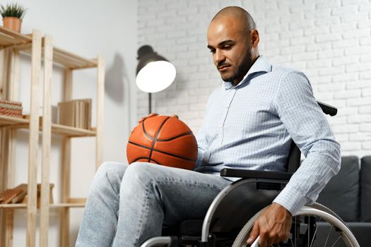 Sad young disabled man in wheelchair holding basketball ball