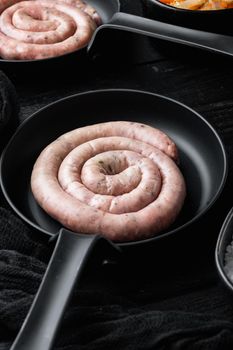 Raw spiral sausage in cast iron frying pan, on black wooden table background