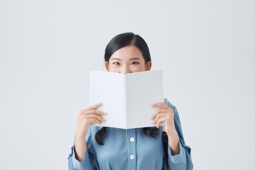 Happy pensive girl holding white notebook, covering half of face, looking attentively at camera,