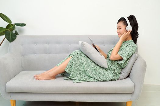 Smiling beautiful asian listening music while using her tablet in the living room