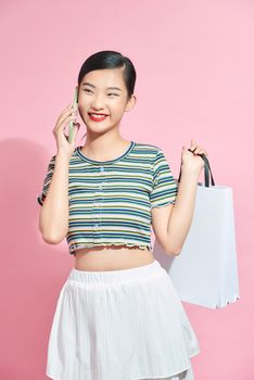 Beautiful Attractive Asian Woman holding shopping bags and calling with mobile phone isolated on pink background