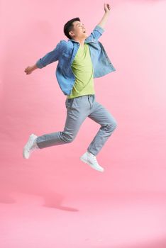 Fun energetic Asian man jumping in mid air isolated on light pink background