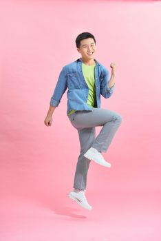 Fun energetic Asian man jumping in mid air isolated on light pink background