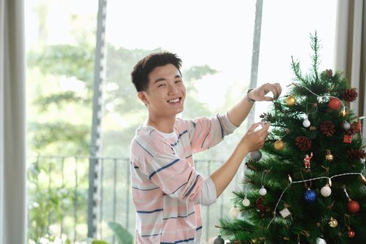 Man putting up Christmas decoration at home holding a  bauble in his hand 