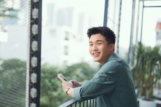 Asian male student texting on smartphone at balcony