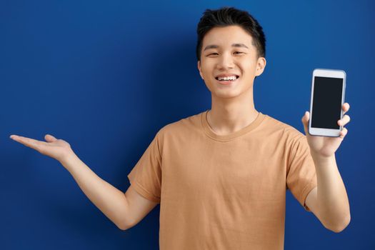 aist-up shot happy enthusiastic man with bristle in purple t-shirt, stretch hand with smartphone showing gadget screen horizontally, smiling pleased,