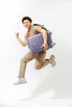 Young excited Asian tourist man with baggage jumping in mid-air ready to travel isolated