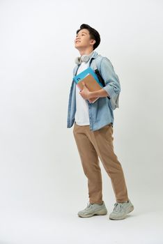 Cheerful young Asian student man with books, headphone, backpack in casual standing over white background.