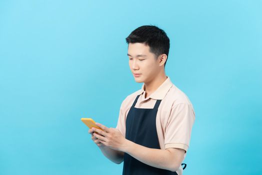 Man with apron sending a message with the mobile over isolated blue background