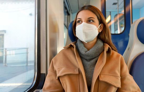 Travel safely on public transport. Young woman with KN95 FFP2 face mask looking through train window. Commuter passenger with protective mask travels sitting on train.