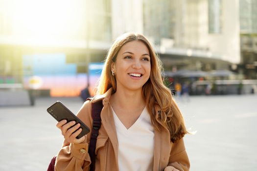 Optimistic happy woman holding a phone looking forward in city