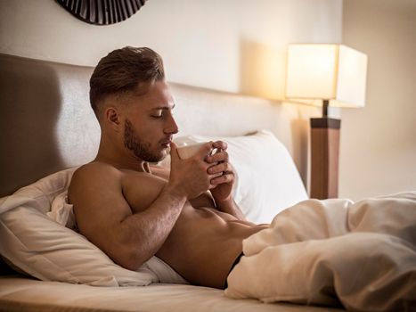 Sexy naked young man on bed with cup