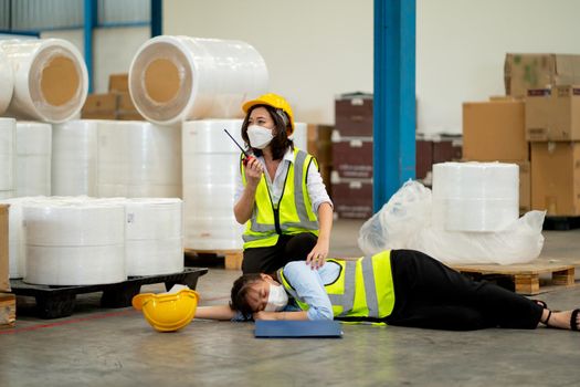 Factory worker woman use walkie talkie ask help to support and save her coworker who faint and lie down on floor during work in warehouse workplace area.