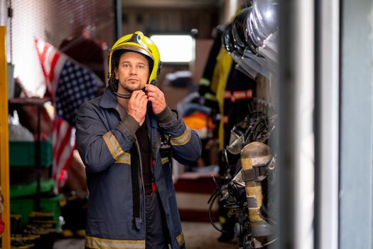 Firefighter man set lock of protective helmet and look at camera also stay in room with accessories for firefighting.