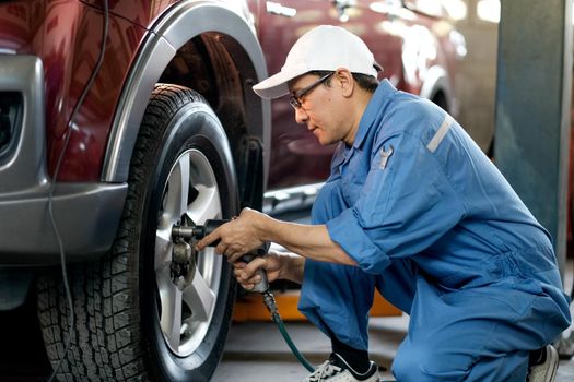 Asian automotive mechanic with white cap and blue uniform is working with replace or fix the problem of car wheel in the garage.