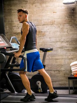 Blond young muscular man running on treadmill in gym