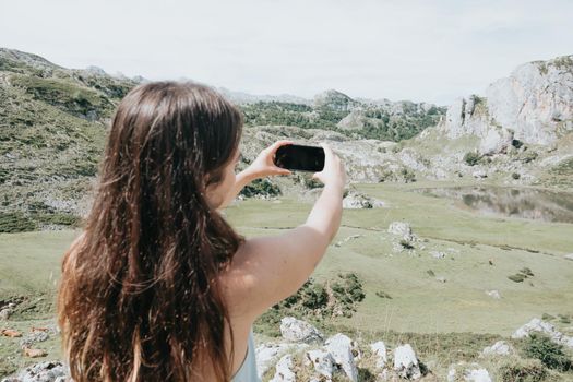 Portrait of young woman taking photos smiling standing at mountain carefree woman.happy traveler hipster girl with windy hair smiling, top of mountains space for text atmospheric moment.