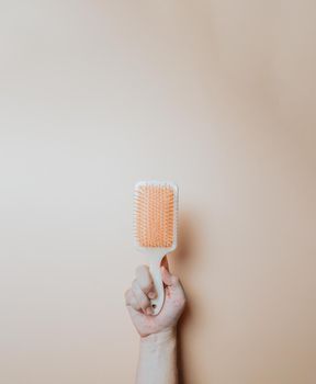 Minimal image of a hand holding an hair comb over a light color background, copy space, minimal image. Hair styling concept, beauty styling