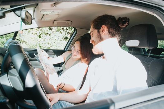 Lovely young couple traveling doing a road trip in car. Road travel, frontal portrait smiling. they are taking a break from driving and looking or checking the map to see the route. Hipster modern couple.