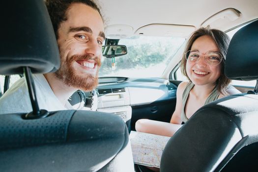 Young hipster couple using a map on a road trip for directions. Reading a map. Cheerful loving couple relaxing on vacation. Trip on route vacation. Happy and smiling to camera. Decision taking