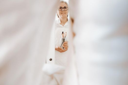 Smiling older woman, proud artist, with grey hair and glasses and many paintbrushes, artistic image