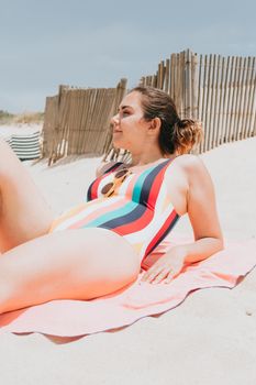 Young woman looks away from camera while taking a sun bath wearing a colorful swimsuit at the beach, travel young holiday concept, copy space, social network, sunglasses user concept