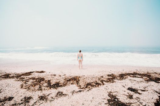 Small young woman in the middle of the beach during a sunny day, mental health concept, solitude