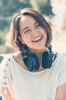 Young woman with short hair having fun while using a big headset to hear music. Outside activities. Happy young girl music enjoy.