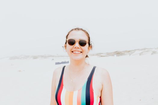 Young woman in a swimsuit and sunglasses smiles to camera during a sunny day at the beach, liberty and holiday concept,portrait