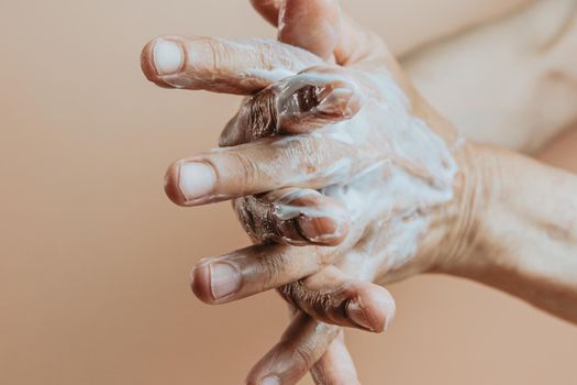 elderly woman rubbing hand cream,close-up, minimal, pastel background copy space, self care concept