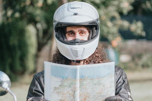 Motorbike travel holding a map while smiling to camera while using a helmet. Travel in bike concept. Long hair man happy digital nomad concepts.